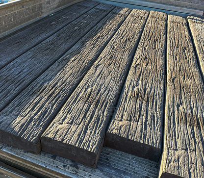 Several long weathered wooden concrete sleepers with a heavily textured, distressed finish arranged on a metal surface.
