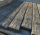 Several long weathered wooden concrete sleepers with a heavily textured, distressed finish arranged on a metal surface.