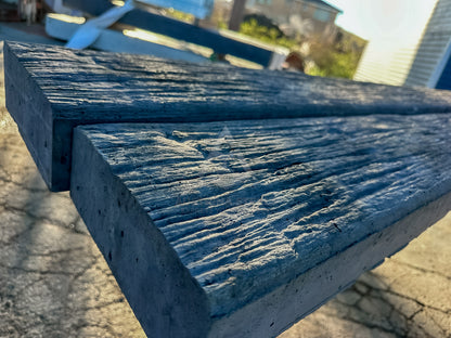 Two rectangular weathered gray concrete or stone pavers with a textured, rustic wood-grain finish, shown outdoors on a paved surface.